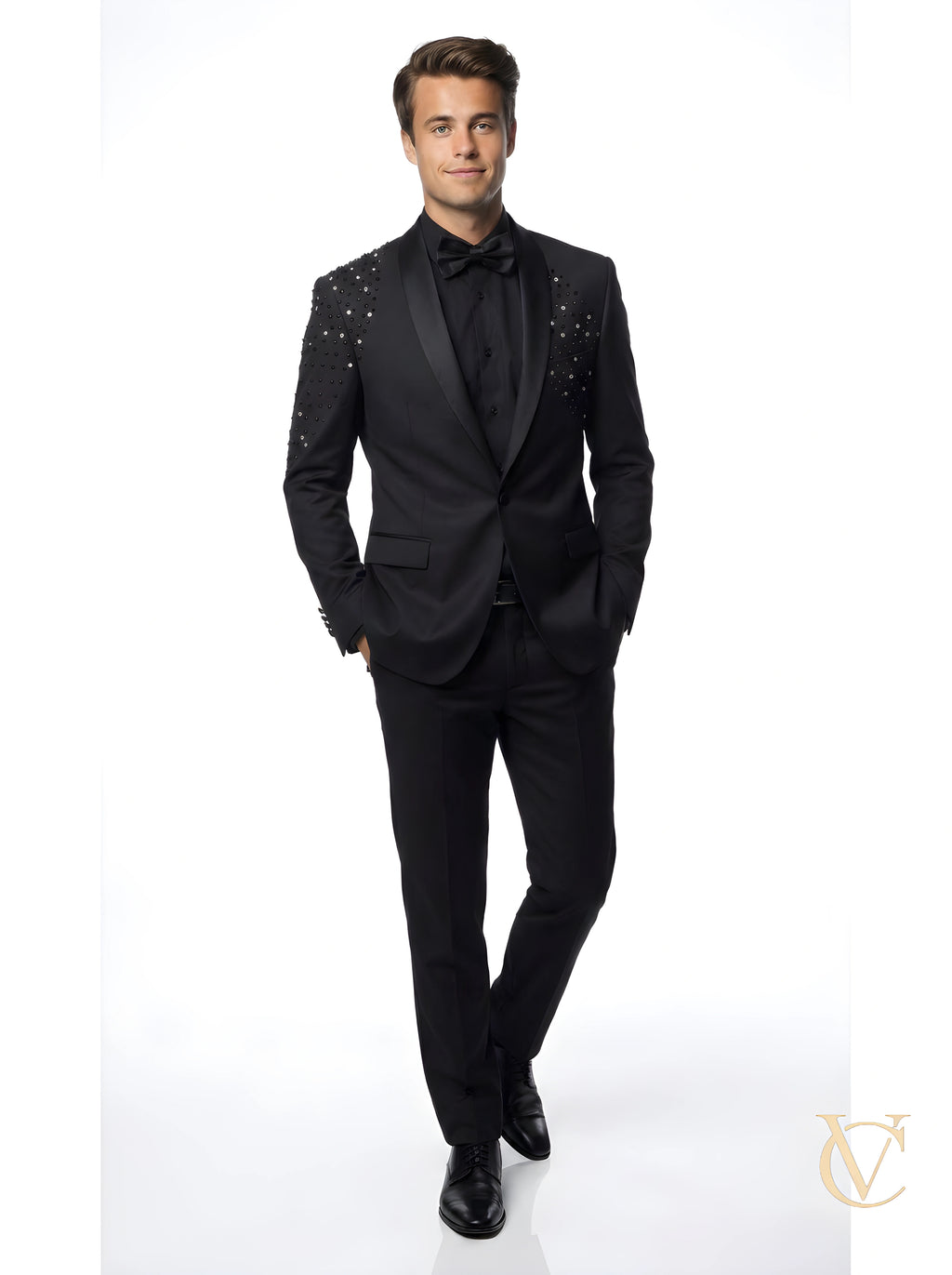 A man wearing a tailored black suit with a satin lapel and crystal embellishments on the shoulders, paired with a black dress shirt and bow tie, Suit - Black | Vellure Couture.