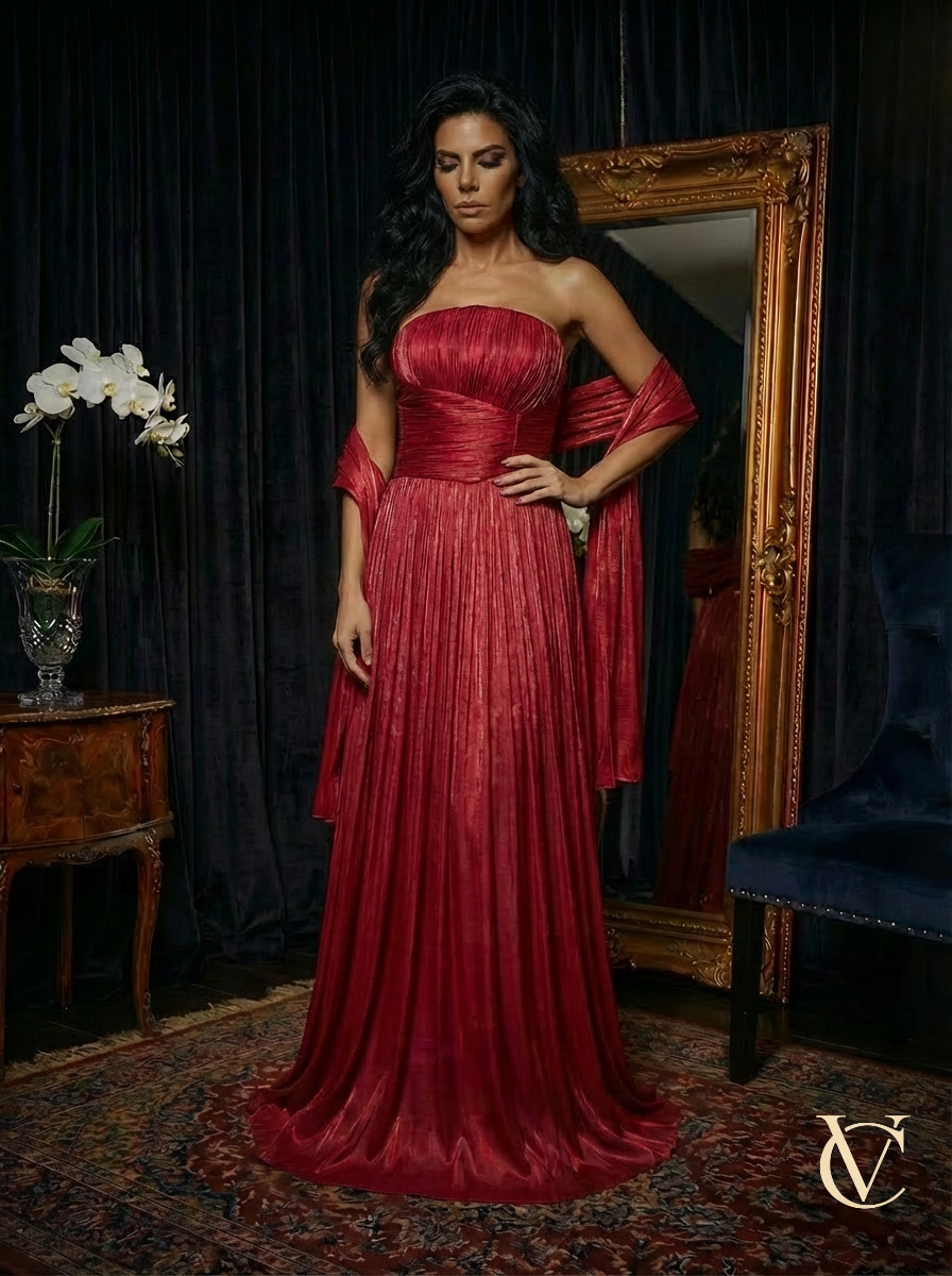 Elegant woman wearing a strapless Pleated Gown - Burgundy | Vellure Couture standing in a luxurious room with a vintage mirror and antique furniture, showcasing luxury evening wear.