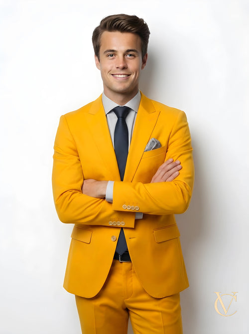 A young man wearing a modern 2-Piece Suit - Yellow | Vellure Couture with a navy tie and light blue shirt, smiling confidently against a white background, showcasing a tailored fit.