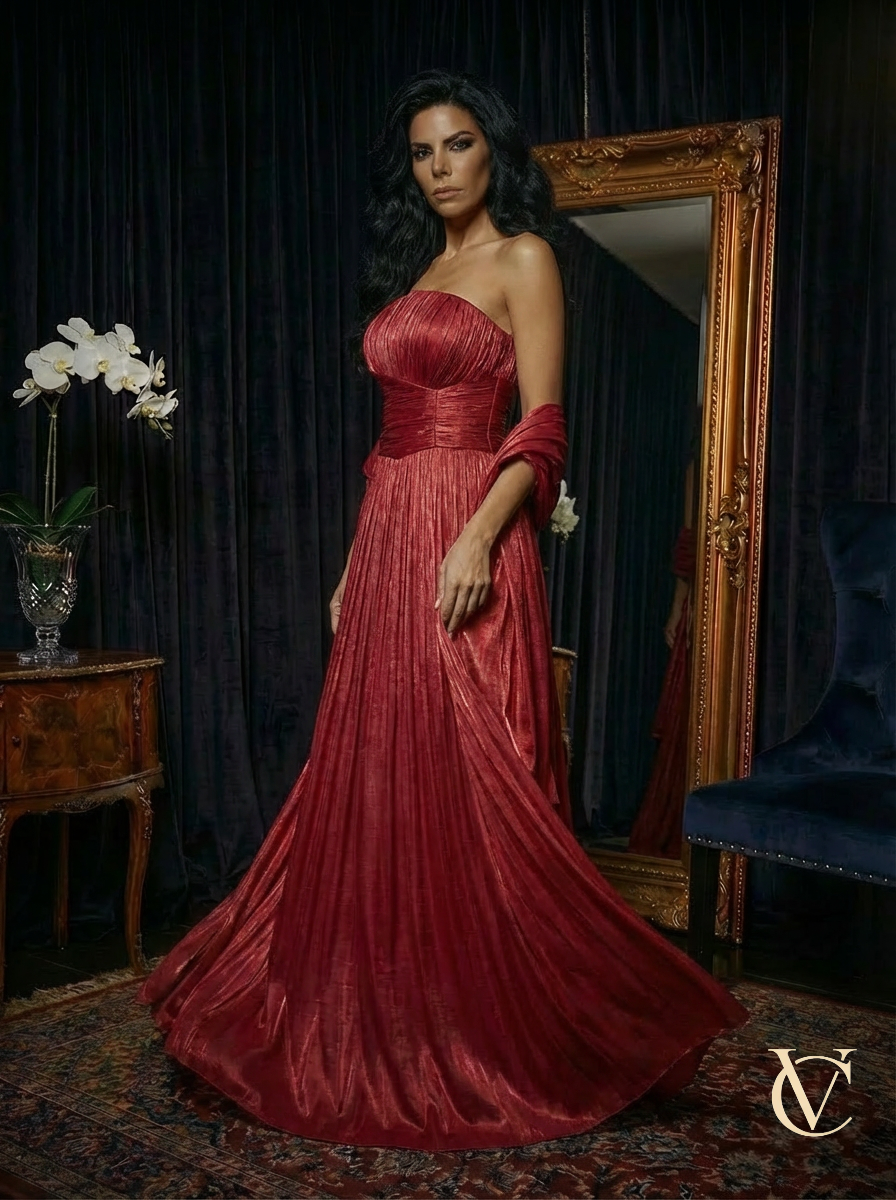 Woman wearing Pleated Gown - Burgundy | Vellure Couture, a strapless, flowing evening dress with rich pleats and a luxurious finish, standing in an elegant room with classic decor.